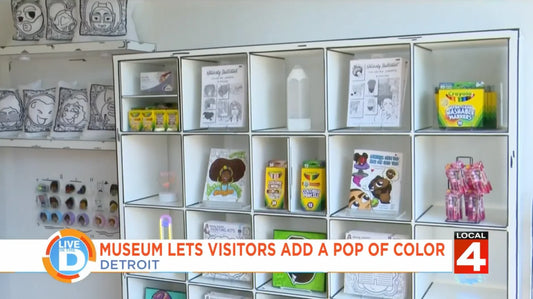 A shelving unit with coloring supplies and artwork is displayed in a museum. Includes boxes of crayons, coloring pages, and various art pieces. Text at the bottom reads, Museum lets visitors add a pop of color - Detroit.