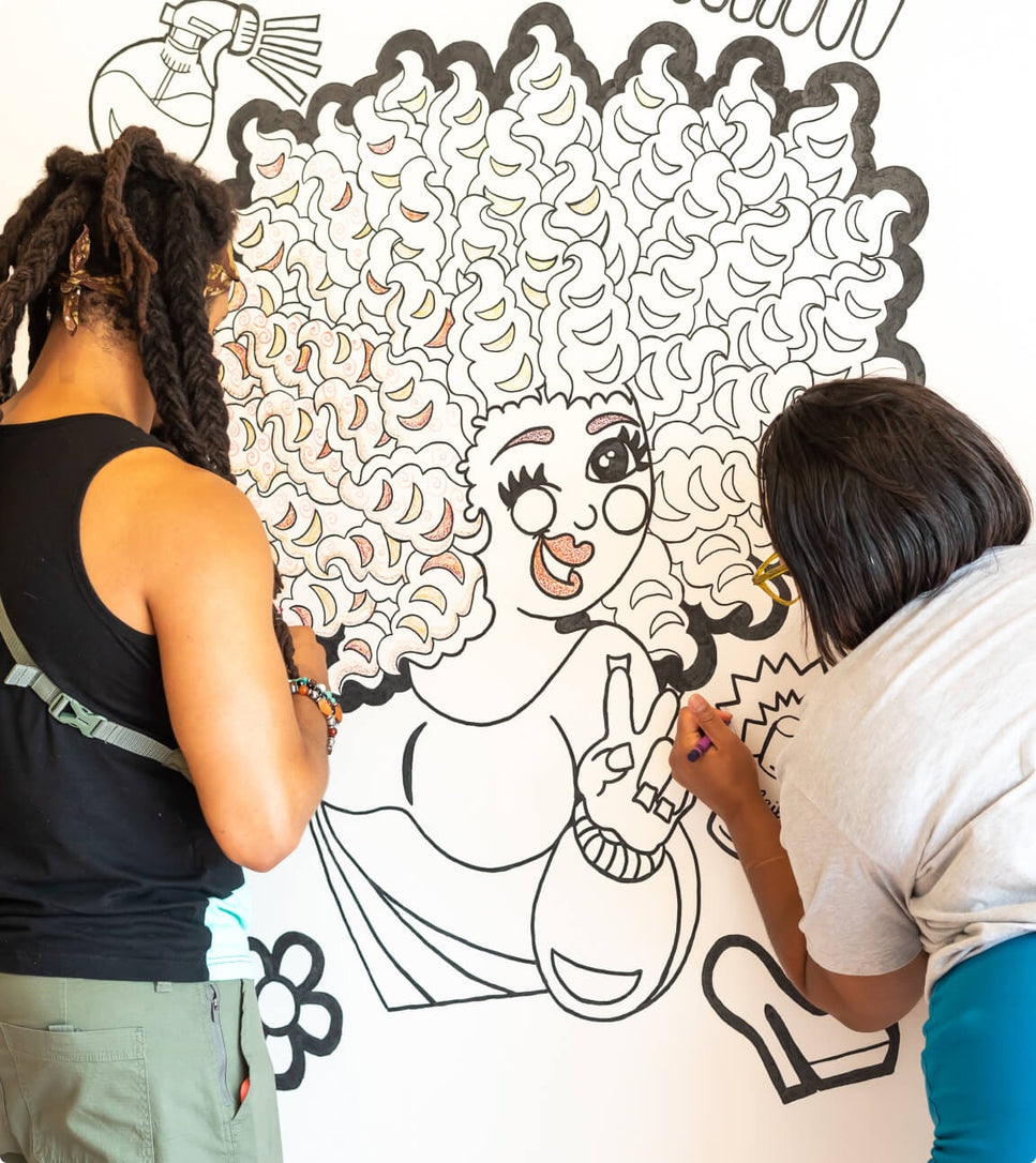 Two people coloring an illustration on the wall at The Coloring Museum