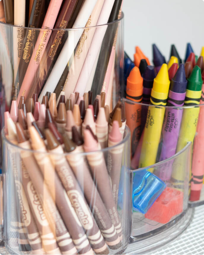 Clear containers filled with skin-tone crayons, colorful crayons, and erasers on display.